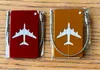Two airplane-shaped luggage tags, one red and one orange, are shown in clear plastic packaging on a wooden surface. Podgląd zdjęcia produktu