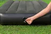 A person's hand is adjusting the valve on an inflatable air mattress that is lying on grass. Náhled obrázku produktu