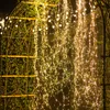 A close-up of cascading string lights with warm white LEDs, draped over a wooden structure and greenery. Produktbild-Vorschau