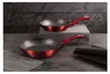 Two red frying pans are displayed on a dark surface in front of a textured black wall. Podgląd zdjęcia produktu
