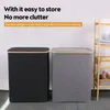 Two laundry baskets with lids, one black and one gray, are shown side-by-side. A wooden shelf unit with towels is visible on the right. Text overlays describe the product's features. Produktbild-Vorschau