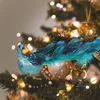 A close-up of a blue peacock ornament with feathers attached to a Christmas tree branch, surrounded by bokeh lights. Produktbild-Vorschau
