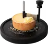 A cheese scraper is shown in use on a round of cheese, resting on a black circular base. Produktbild-Vorschau