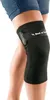 A person wearing a black knee brace with a strap and logo. Produktbild-Vorschau