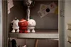 Three small, stylized figures resembling sports balls with legs are placed on a shelf inside a locker. A trophy is visible in the background. Produktbild-Vorschau