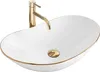 A white oval countertop sink with a gold faucet and drain. Náhľad obrázku produktu