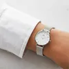 A person's wrist wearing a silver watch with a white face, partially covered by a white shirt sleeve. Voir les images du produit