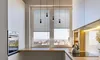A modern kitchen with a window overlooking a city view, featuring blinds, pendant lights, and kitchen appliances. Produktbild-Vorschau