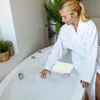 A woman in a white bathrobe is reaching into a bathtub with a bath seat installed. Voir les images du produit