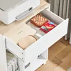 A close-up view of an open drawer of a white printer stand, revealing various items stored inside, including a printer, a wooden chessboard, and a red tin box. Podgląd zdjęcia produktu