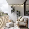 A balcony decorated with plants and outdoor furniture, with a view of houses and trees in the background. Podgląd zdjęcia produktu