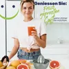 A woman is holding a glass of freshly squeezed juice, with grapefruits and a juicer on the counter. Produktbild-Vorschau