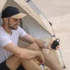 A man is sitting inside a tent, holding a small black Bluetooth speaker. Voir les images du produit