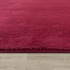A close-up view of a red rug on a wooden floor. Produktbild-Vorschau