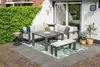 An outdoor patio set with a sectional sofa, coffee table, and bench on a rug with a leaf pattern, next to a green ivy wall and a white brick house. Produktbild-Vorschau