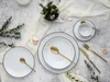 A table setting with white plates, gold cutlery, and a small vase of greenery. Podgląd zdjęcia produktu