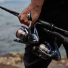 A person holding two fishing reels and a fishing rod near the water. Produktbild-Vorschau