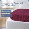 A close-up view of a burgundy fitted sheet draped over a white mattress, with text overlays highlighting product features. Produktbild-Vorschau