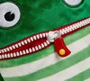 A close-up of a green plush toy with a zipper that resembles a mouth, and a red zipper pull with a yellow dot. Produktbild-Vorschau