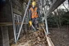 A construction worker is using a leaf blower to clear debris from scaffolding next to a building. Podgląd zdjęcia produktu