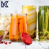 Jars of pickled vegetables on a white wooden surface, with a red lid in the foreground. Podgląd zdjęcia produktu