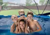 A family is posing for a photo in a swimming pool, with a backyard visible in the background. Anteprima dell’immagine prodotto