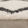 Close-up view of a fluffy rug with a geometric pattern on a wooden floor. Produktbild-Vorschau
