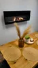 A modern living room setting with a wall-mounted ethanol fireplace above a wooden dining table. Anteprima dell’immagine prodotto