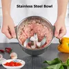 A person is holding a stainless steel bowl filled with minced meat and a food chopper blade inside. There are also some ingredients like chili peppers and garlic on the table. Produktbild-Vorschau