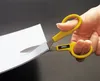 A hand is using yellow-handled scissors to cut a piece of white paper. Anteprima dell’immagine prodotto