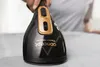 A hand holding a black and gold handheld steamer over a gray fabric surface. Podgląd zdjęcia produktu