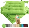 A stack of four green seat cushions with ties, displayed on a white background. A product tag is attached to the top cushion. Voir les images du produit