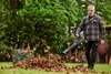 A man is using a leaf blower to clear leaves in a garden. Produktbild-Vorschau