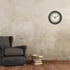 A clock on a wall above a chair and books. Anteprima dell’immagine prodotto