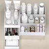 A white organizer filled with various cosmetic products, including bottles, jars, brushes, and a small drawer, placed on a light gray surface. Produktbild-Vorschau