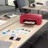 A red Canon printer is shown on a desk with papers and a smartphone. Anteprima dell’immagine prodotto