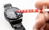 A hand is holding a tube with the word 'REPAIR' on it, applying something to a black watch. Produktbild-Vorschau
