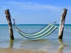 A striped hammock is suspended between two wooden posts in the shallow water of a beach. Produktbild-Vorschau