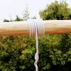 A thick white rope is wrapped around a wooden beam, with lush green foliage in the background. Podgląd zdjęcia produktu
