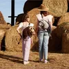 Two people wearing hobby horse backpacks in a barn with hay bales. Náhľad obrázku produktu