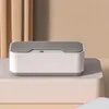 A small, white and gray electronic device sits on a pale pink pedestal, with beige curtains in the background. Produktbild-Vorschau