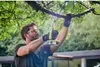 A man is using a Ryobi saw to cut a tree branch outdoors. Podgląd zdjęcia produktu