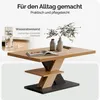 A modern coffee table with a unique base design, shown with decorative vases and a book on top, and a close-up inset showing water droplets on a surface. Produktbild-Vorschau