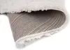 A close-up view of the underside of a rolled-up rug, showing the woven backing and the fluffy texture of the pile. Voir les images du produit