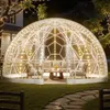 A transparent geodesic dome tent set up in a backyard at night, illuminated by string lights, with outdoor furniture inside. Anteprima dell’immagine prodotto