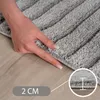 A hand is shown pressing down on a thick, gray rug to demonstrate its plushness and thickness. Voir les images du produit