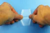 Two hands are holding a piece of clear tape against a blue background. Produktbild-Vorschau