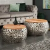 Two round coffee tables with wooden tops and mosaic-style metal bases are placed in a living room setting next to a tufted gray sofa.