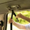 A person's hands are shown attaching a black strap with a carabiner clip to a car's interior grab handle. Náhľad obrázku produktu