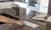 A person's hand is pressing a pop-up electrical outlet on a kitchen counter next to an open cookbook. Anteprima dell’immagine prodotto